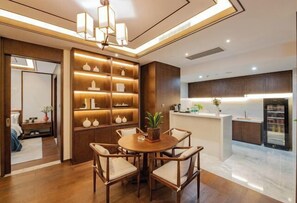 A modern dining area with a round table and chairs, a built-in shelving unit with decorative items, and a kitchen area with a countertop and cabinets. - Hanrun 1882 Hotel (Nanjing)
