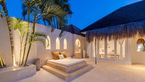 A bedroom with a bed, a small table, and a chair. There are palm trees and a thatched roof structure. - Villa Casa Bocami Canggu By Azure Near Finns (Canggu)
