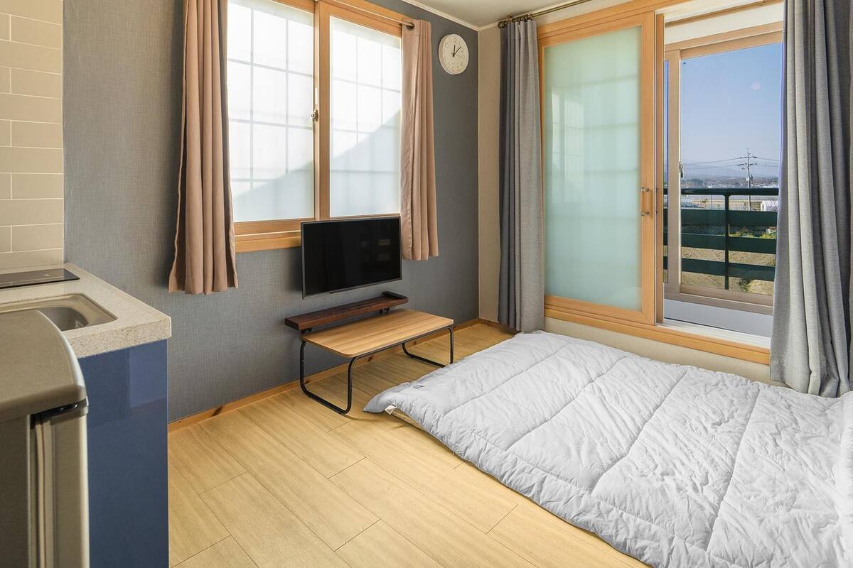 A compact hotel room with a bed, a small table, a TV, and a window with curtains.