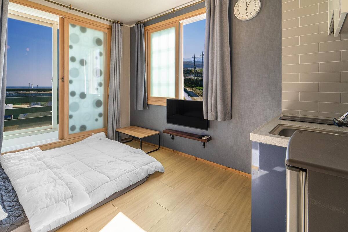 A compact room with a bed, a small table, a TV, and a kitchen area with a sink.