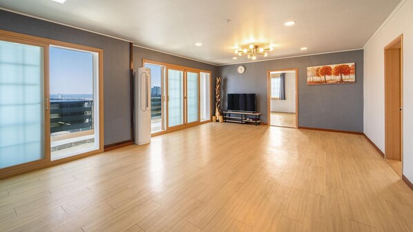 A spacious living room with large windows, a flat-screen TV, and a ceiling light fixture. - Gangneung Basecamp Pension (Gangneung)