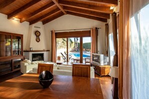 Uma sala de estar ampla com teto de madeira, lareira, vista para a piscina e televisão.