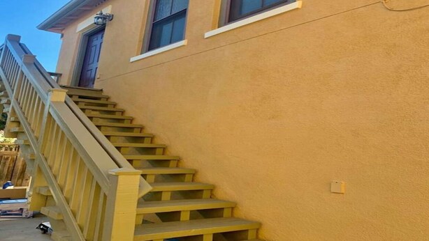 Un edificio con fachada amarilla, una escalera de madera y una ventana.