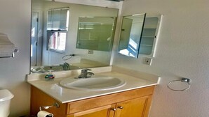 Un baño con lavamanos blanco, tocador de madera, un espejo grande y un aro para toallas.