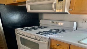 Una cocina con un refrigerador negro, una estufa blanca y un microondas sobre la estufa.