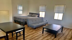 Un dormitorio con una cama, un sofá gris, dos mesitas negras y suelo de madera.