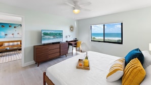 Een slaapkamer met een bed, bureau, televisie en uitzicht op de oceaan.