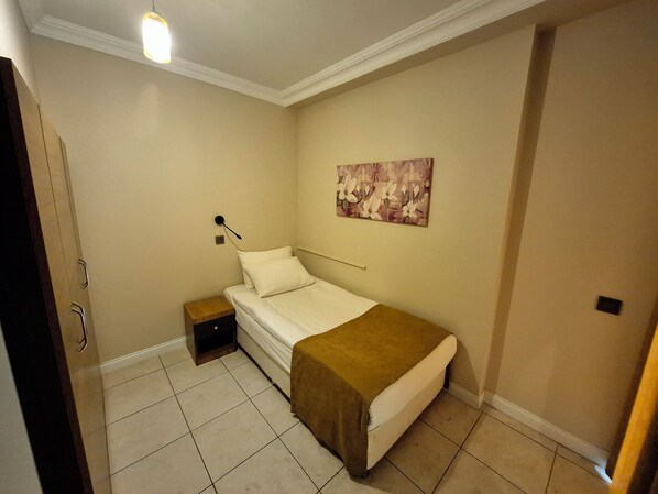 Un dormitorio pequeño y ordenado con una cama individual, una mesita de noche, una lámpara de pared y un cuadro con motivos florales.