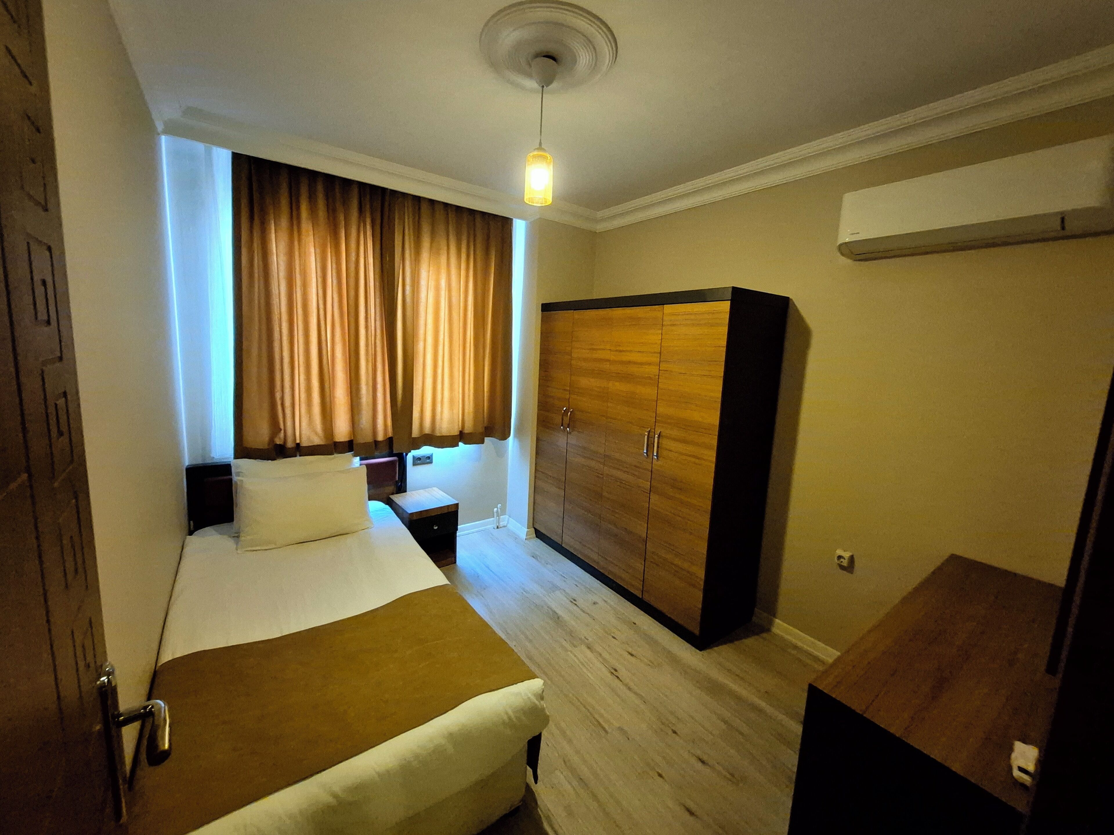Habitación de hotel con cama, armario, mesita de noche y aire acondicionado.