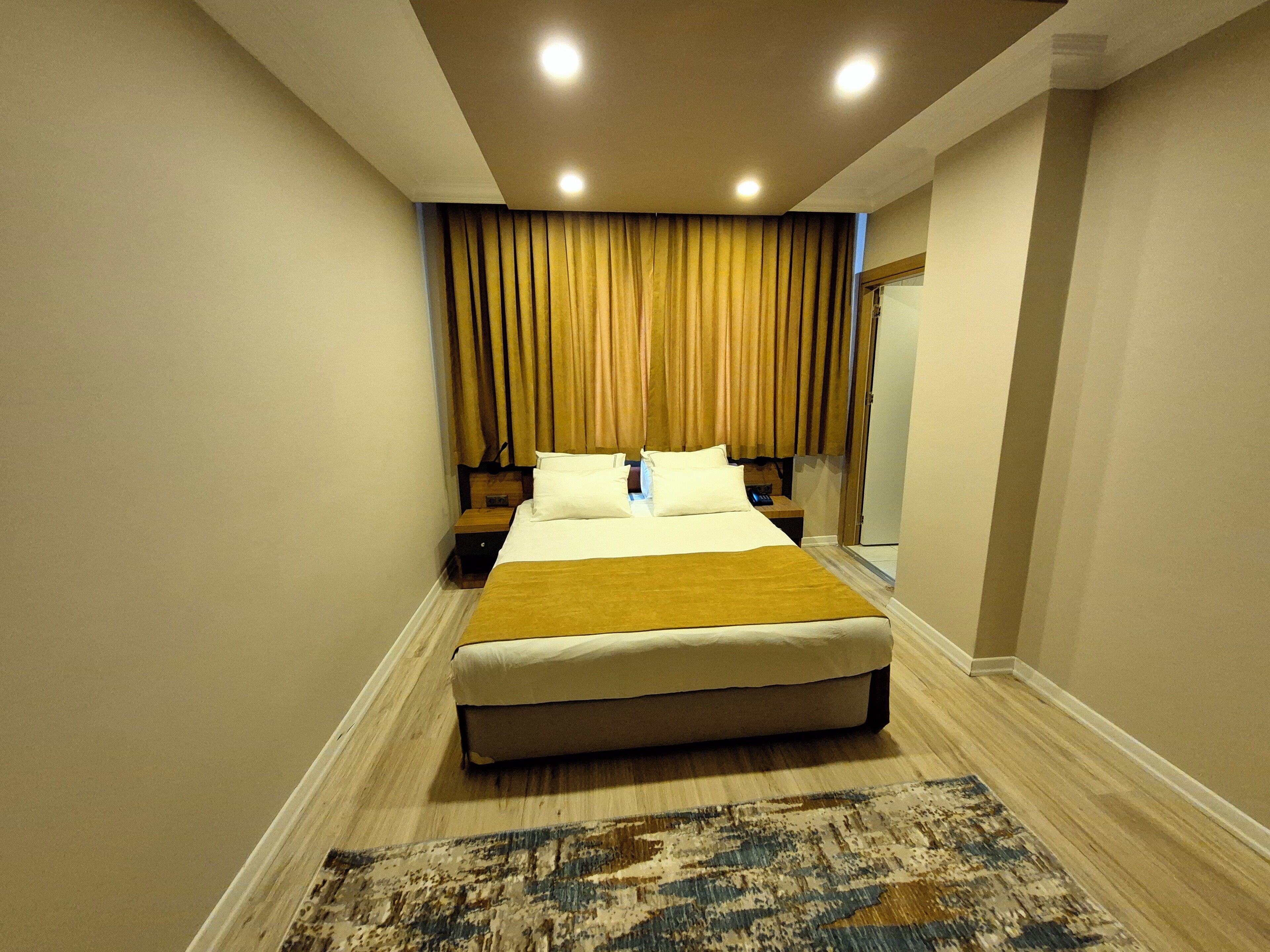 A hotel room with a large bed, a nightstand, a mirror, and a wooden floor.