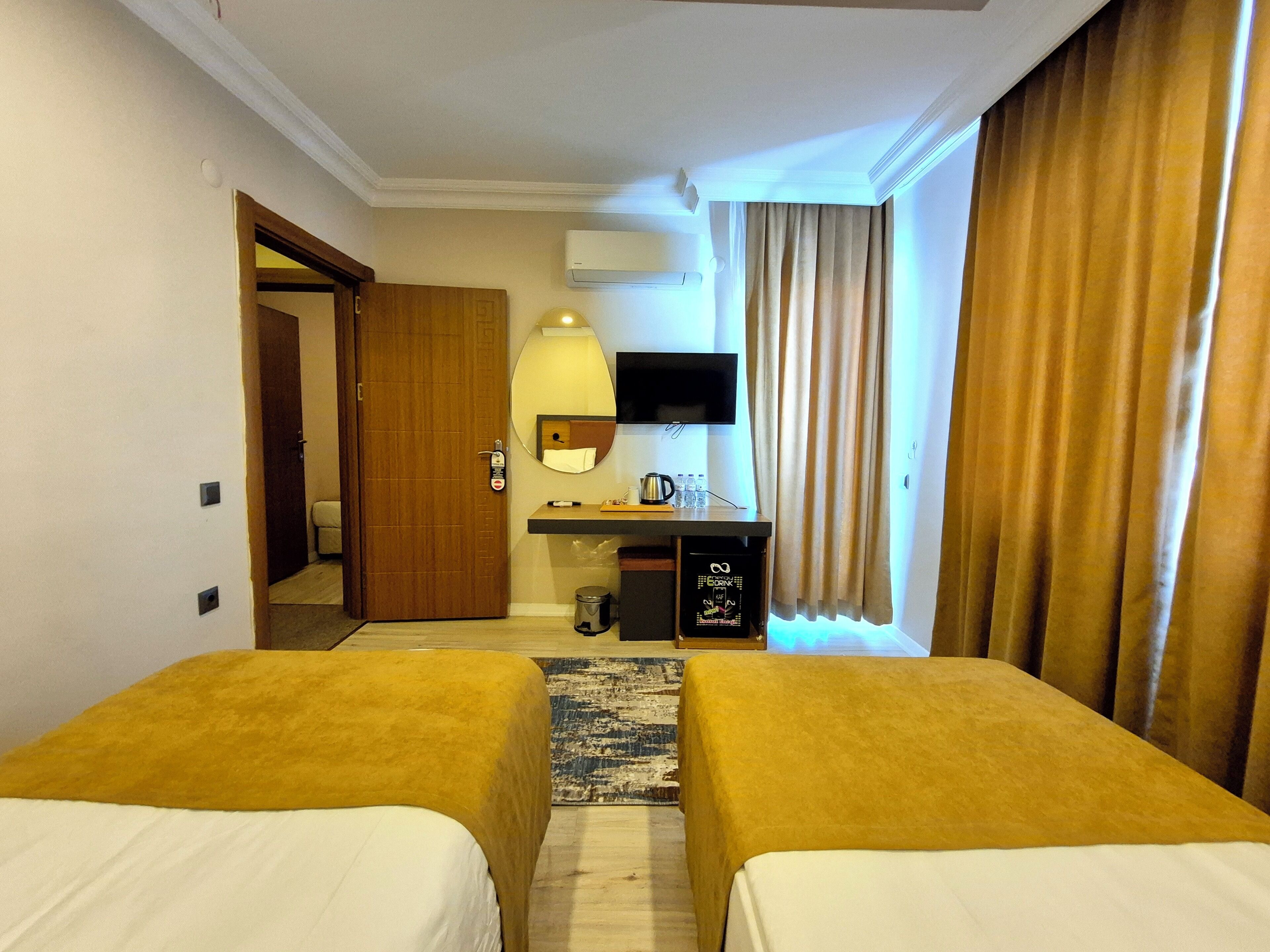 A hotel room with two beds, a desk with a mirror, a TV, and a window with curtains.