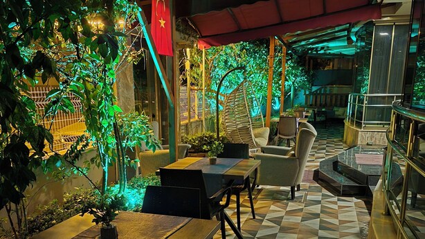 Un espacio al aire libre con mesas y sillas, rodeado de follaje y un suelo con diseño.