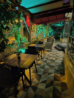 Un espace extérieur aménagé avec des tables et des chaises, entouré de verdure et doté d’un sol à motifs.