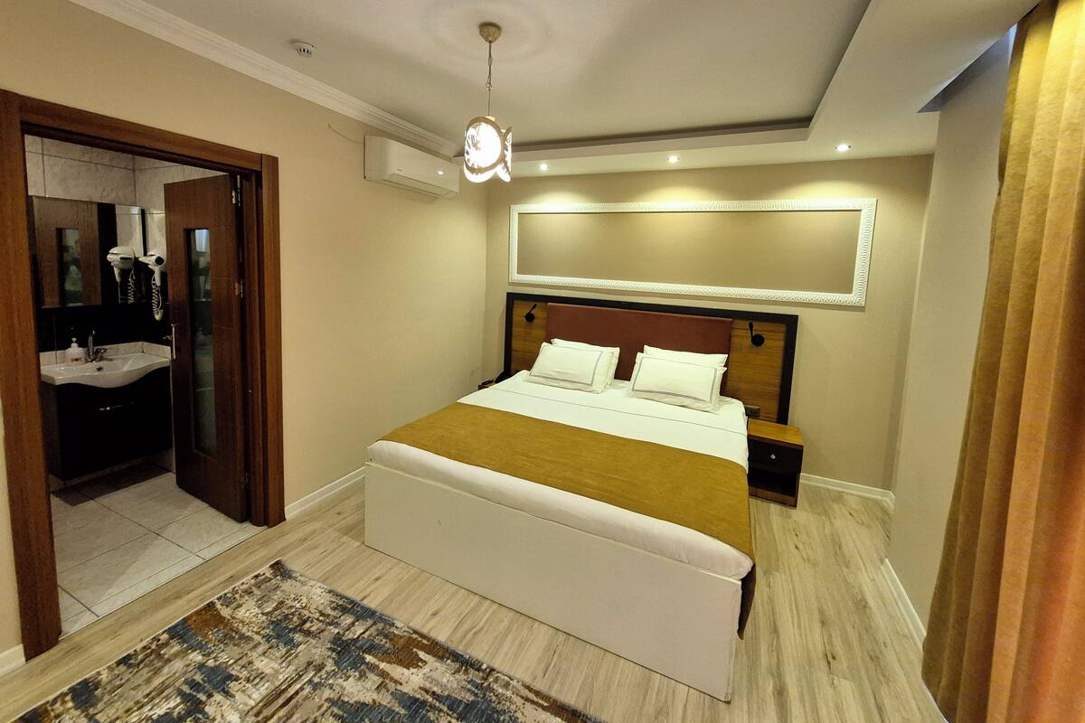 Ein Hotelzimmer mit einem großen Bett, einem Nachttisch, einem Spiegel, einer Deckenleuchte und einem durch eine offene Tür einsehbaren Badezimmer.