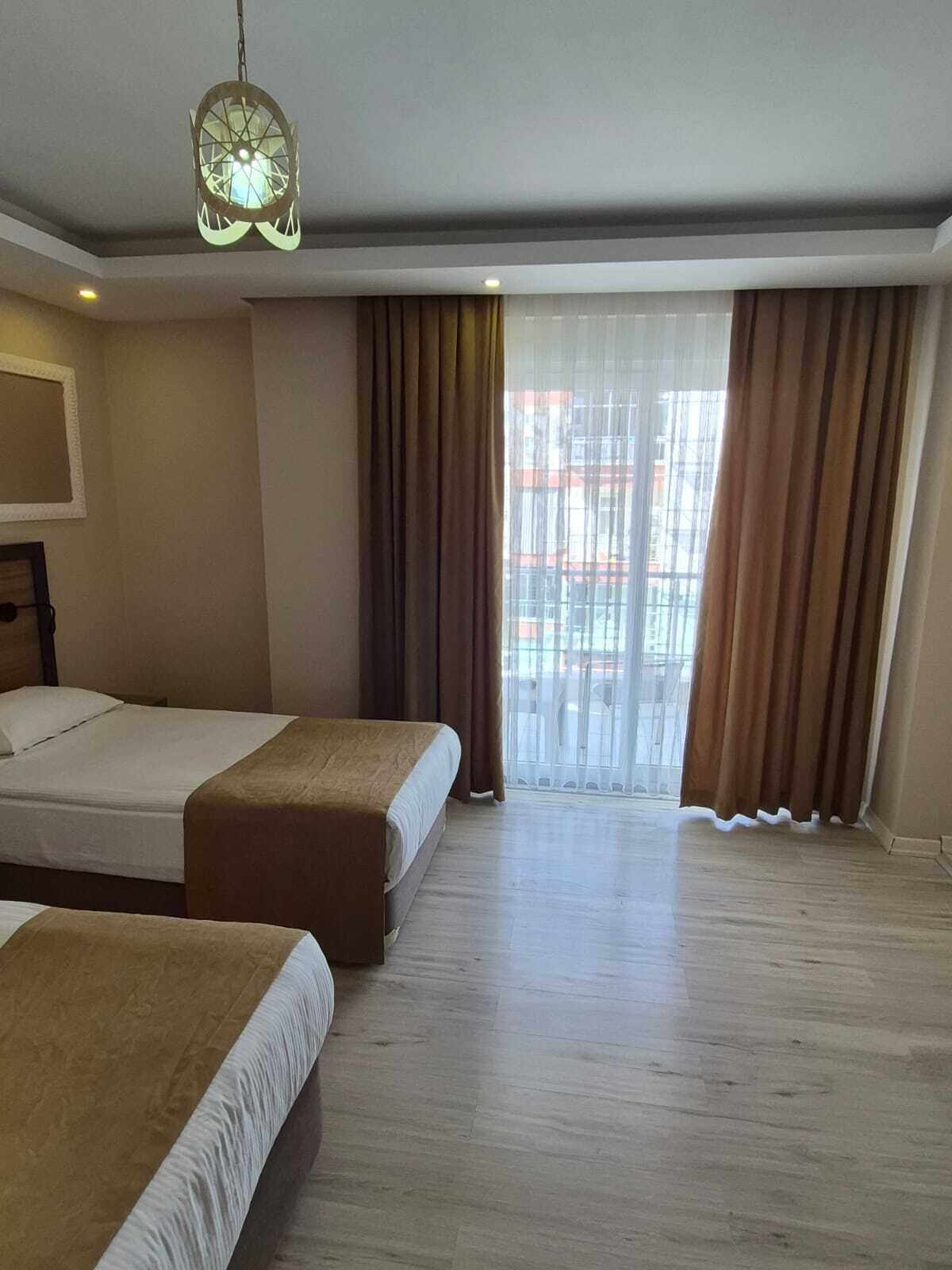 A hotel room with two beds, a large window with curtains, and a hanging light fixture.