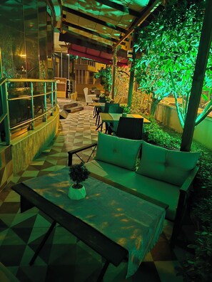 Un espacio de estar al aire libre con piso a cuadros, cojines verdes y una jardinera con un árbol pequeño.