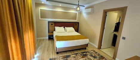 A modern hotel room with a large bed, a wooden headboard, a patterned rug, and a ceiling light fixture.