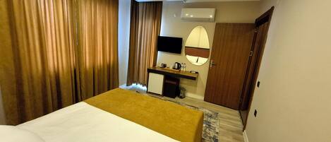 A hotel room with a bed, a desk, a mirror, and an air conditioning unit.