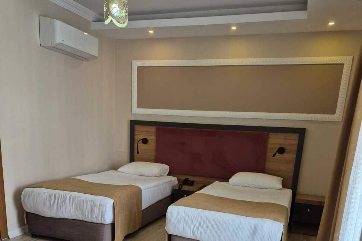 Ein Hotelzimmer mit zwei Einzelbetten, einem Holzkopfende, einer Deckenleuchte und einem großen Fenster.