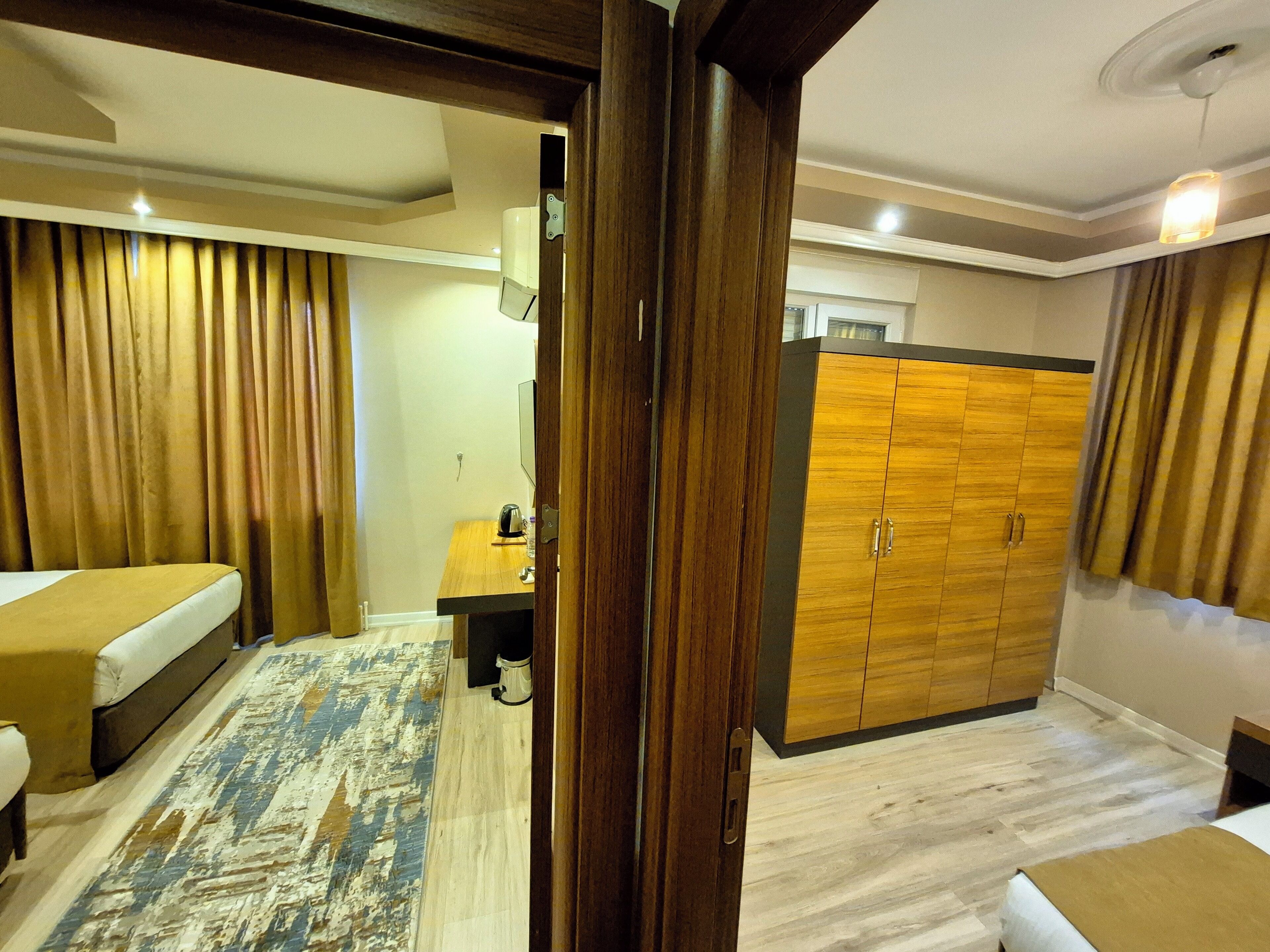 Une chambre d’hôtel avec un lit, un bureau, une armoire et une grande fenêtre avec des rideaux.