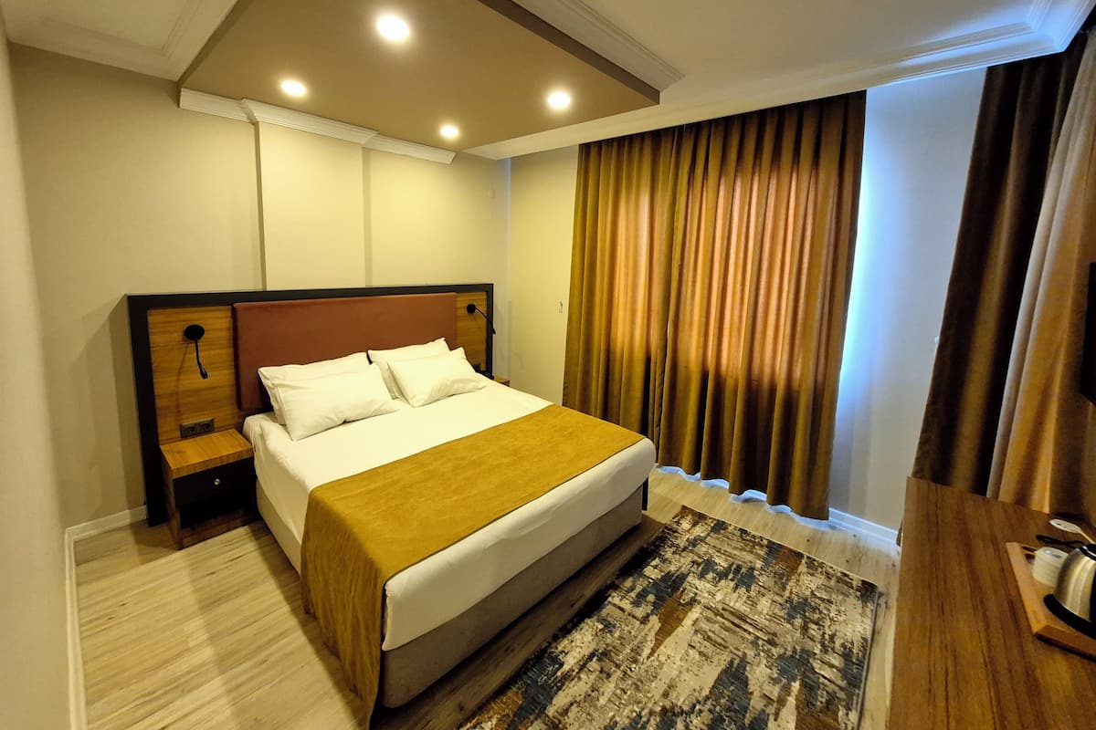 Ein Hotelzimmer mit einem Bett, Nachttischen, einem Holz-Kopfteil, einem gemusterten Teppich und einem Fenster mit Vorhängen.