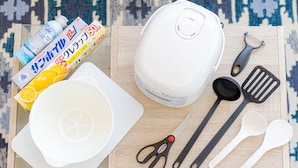 A wooden table with kitchen utensils, a white bowl, a pair of scissors, and a package of orange juice.