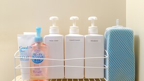 A bathroom shelf with various toiletries including a bottle of shampoo, conditioner, body soap, and a bar of soap.