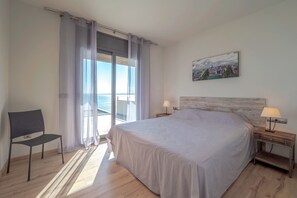 A bedroom with a large bed, a chair, a nightstand with a lamp, and a painting on the wall. - VILLA VELAZQUEZ Roses (Rosas / Roses)