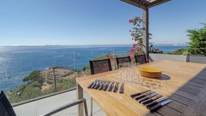 Mesa de madera dispuesta para comer, con vista al mar y montañas al fondo.