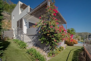 Ein modernes, zweistöckiges Haus mit überdachter Veranda und einem Garten mit blühenden Pflanzen.