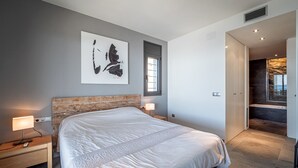 Un dormitorio moderno con una cama grande, mesitas de noche con lámparas, una ventana y vistas a un balcón.