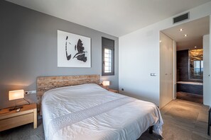 A modern bedroom with a large bed, bedside tables with lamps, a window, and a view of a balcony. - VILLA VELAZQUEZ Roses (Rosas / Roses)