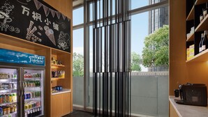 A hotel lobby with a refrigerated beverage display, a coffee machine, and a large window with a view of trees. - Fairfield by Marriott Shenzhen Shenshan Special Cooperation Zone (Shanwei)
