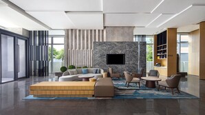 A modern living room with a sectional sofa, a coffee table, and a TV mounted on a marble wall. - Fairfield by Marriott Shenzhen Shenshan Special Cooperation Zone (Shanwei)