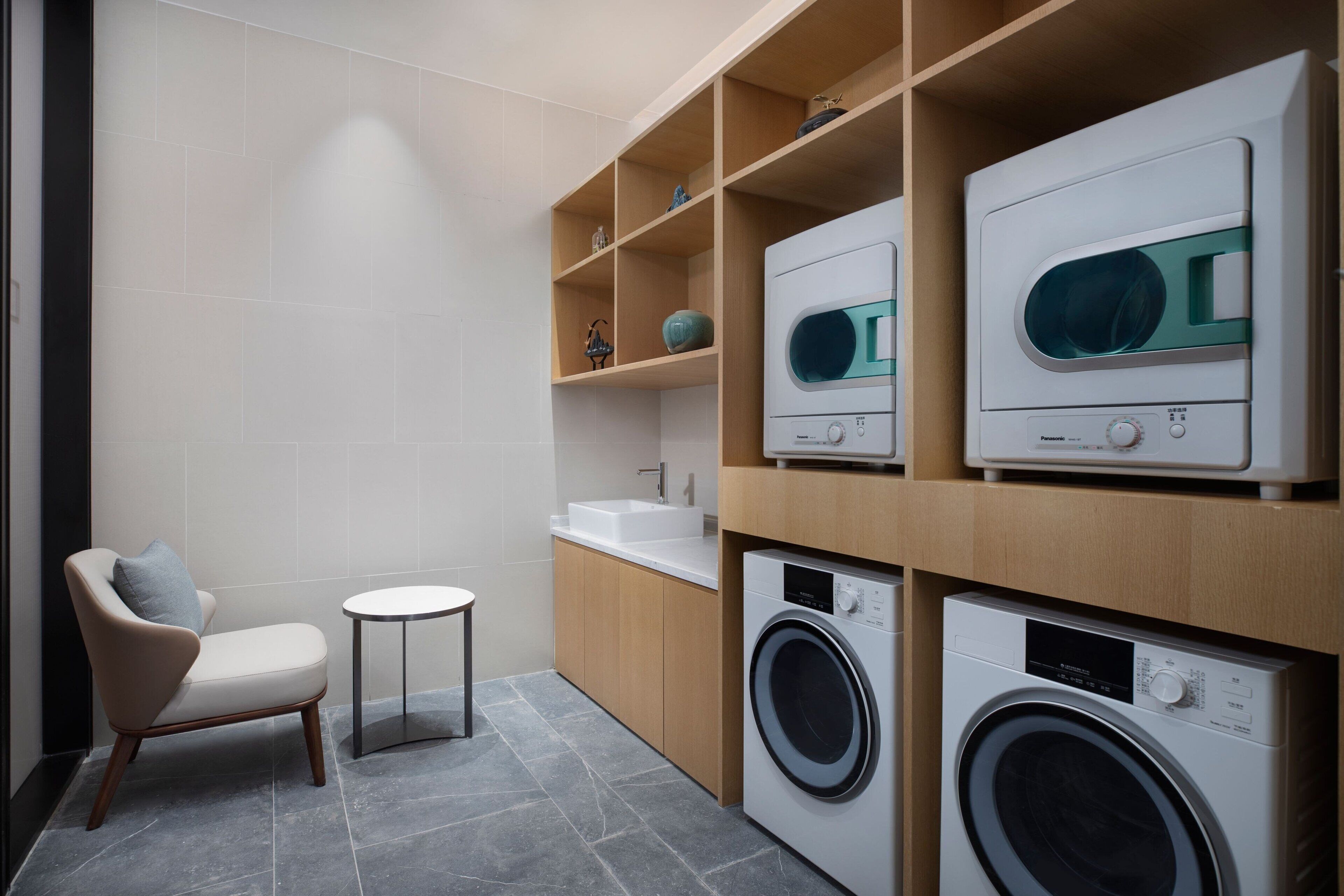 A modern laundry room with built-in washers and dryers, a small round table, and a chair.