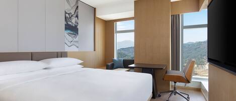 A hotel room with a large bed, a desk, a chair, and a TV.