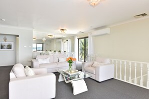 A spacious living room with a white sofa set, a glass coffee table, and a view of the outdoors.