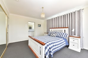 Een slaapkamer met een bed, nachtkastjes, een spiegel, een foto aan de muur en een kroonluchter.