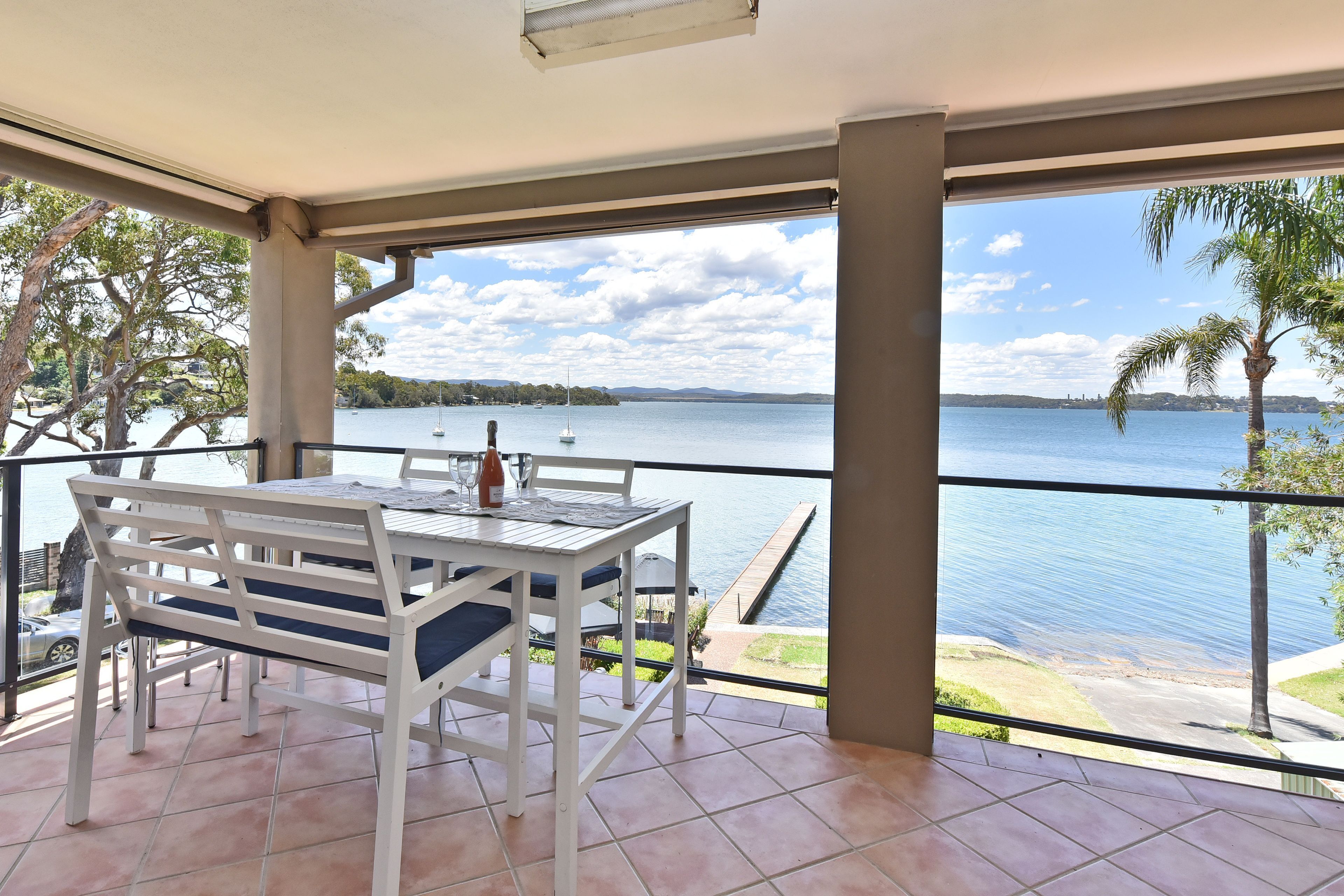 A balcony with a table and chairs, overlooking a body of water with boats and a dock.