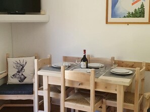 Una mesa de comedor de madera dispuesta con platos, vasos y una botella de vino. Hay un cojín con una imagen de un ciervo en el banco junto a la mesa.