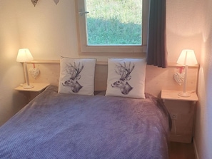 A bedroom with a bed, two nightstands, two lamps, and two decorative pillows with deer head designs. - Cozy 2-Room Apartment for 4 in Prime Ski-In/Ski-Out Location, Near Lifts and Shops (Valfréjus)