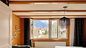 A bedroom with a large window, wooden walls, a green sofa, a bed, and a hanging light fixture. - THE Best Valley View •  Swiss Charm • Free Parking (Lauterbrunnen)