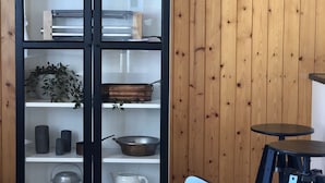 A wooden-paneled room with a glass-fronted cabinet containing kitchenware. There is a wooden table with chairs and a small round table with a stool. - THE Best Valley View •  Swiss Charm • Free Parking (Lauterbrunnen)
