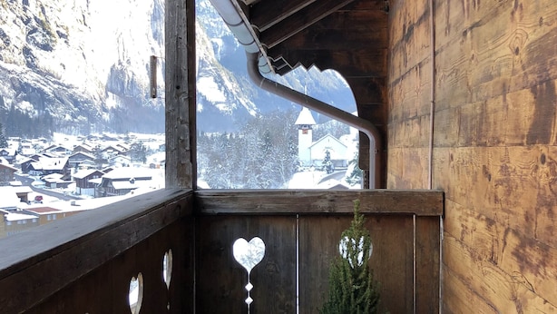 A wooden balcony with a view of a snowy mountain and a village below. - THE Best Valley View •  Swiss Charm • Free Parking (Lauterbrunnen)