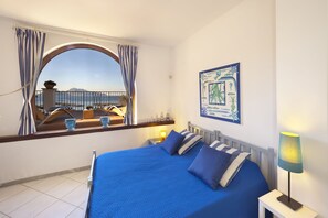 A bedroom with a large bed, a view of the sea, and a balcony with a railing.