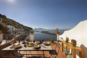 A terrace with a table set for dining, overlooking a coastal area with buildings and the sea.