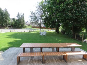 Een picknicktafel met bankjes in een groene achtertuin met bomen en een hek.