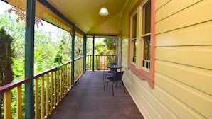 A covered porch with a table and chairs, a railing, and a window with shutters.