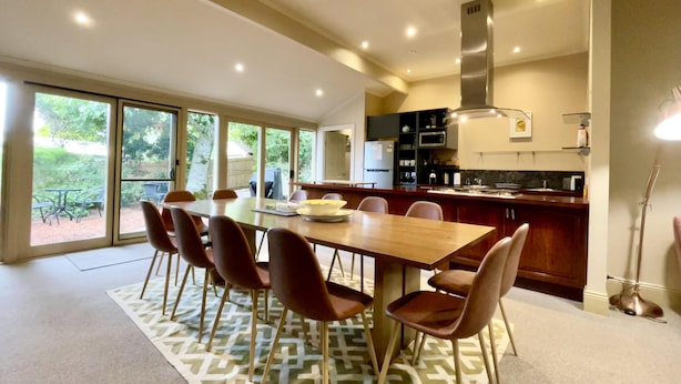 A modern kitchen with a large island, a dining area with a wooden table and chairs, and a view of the outdoors through large sliding doors.