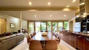 A modern kitchen with a dining area, featuring a long wooden table, brown chairs, and a patterned rug.